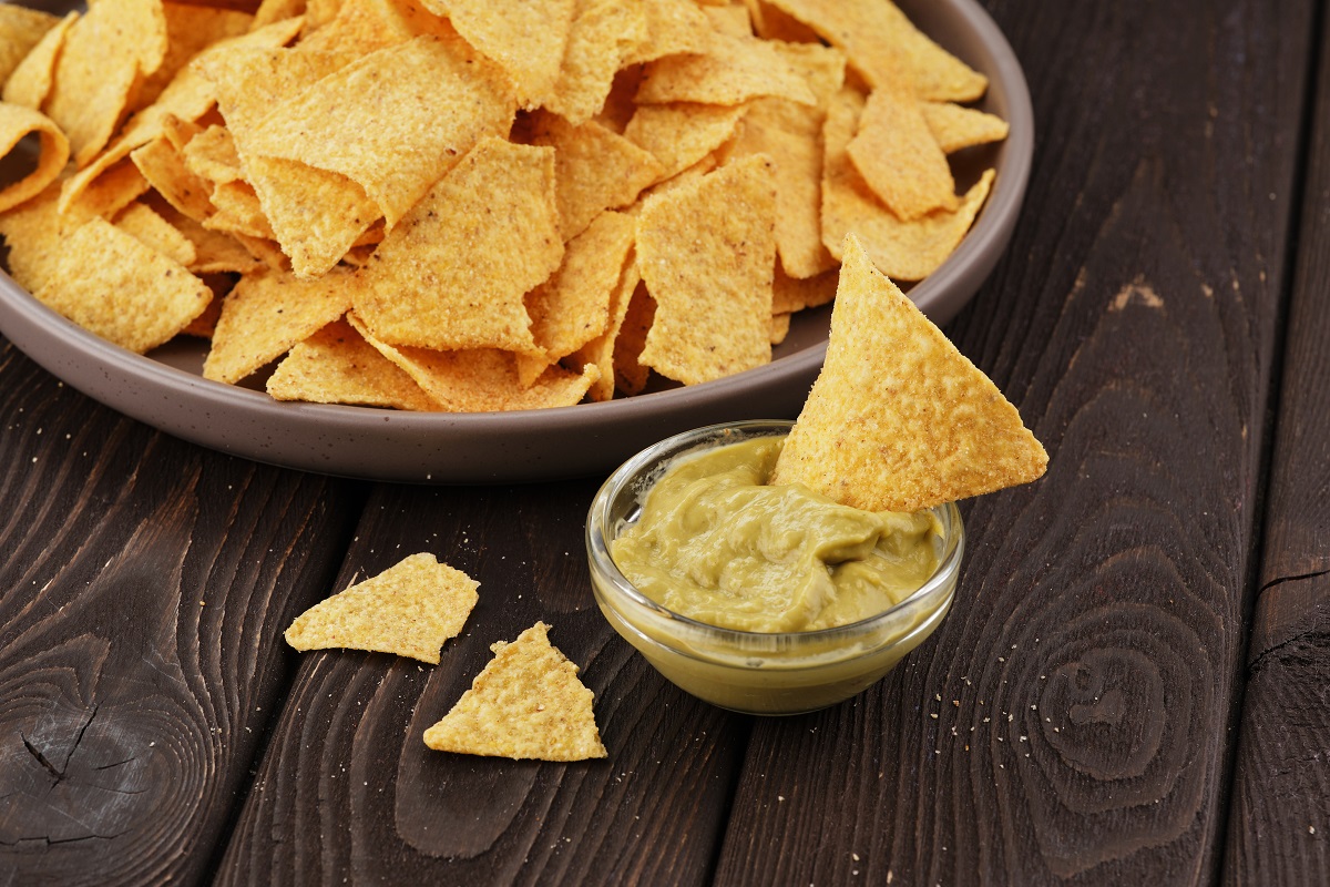 Nachos in a brown plate with guacomole on a dark brown wooden background. Mexican food concept, nachos, guacamole.